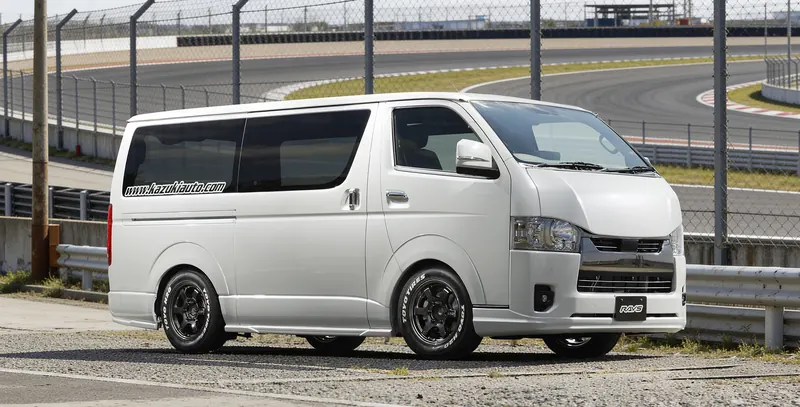 黒いレーシングホイールを装着した白いハイエース、サーキットコースを背景にしたスポーツスタイル